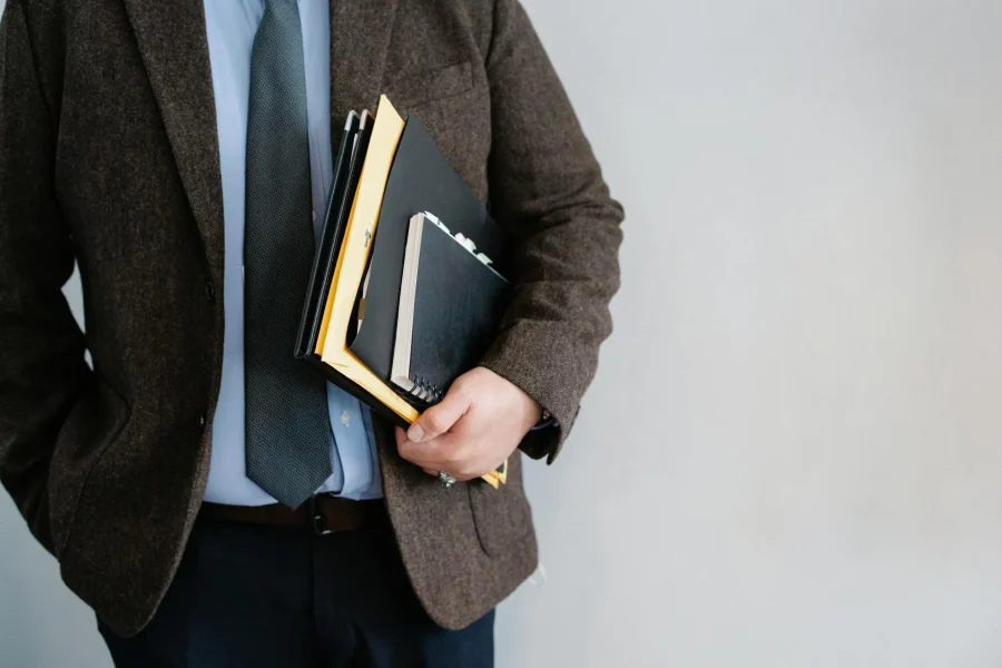 Hombre con traje sosteniendo carpetas y cuadernos, símbolo de la gestión administrativa y legal en la empresa.