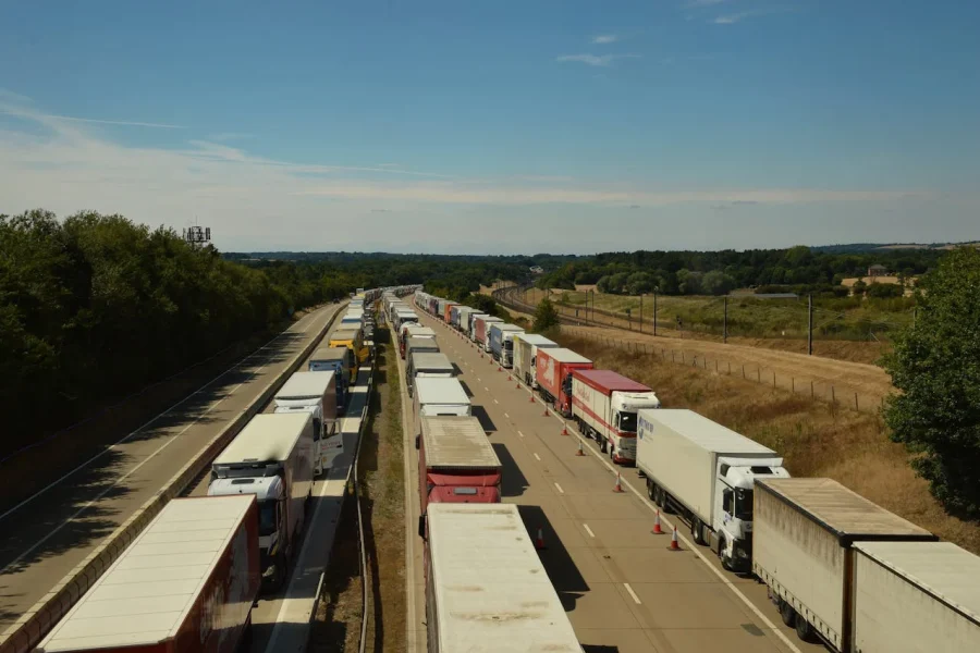 Vista aérea de una larga fila de camiones detenidos en una autopista, desviados a un solo carril, en un entorno rural con cielo despejado.