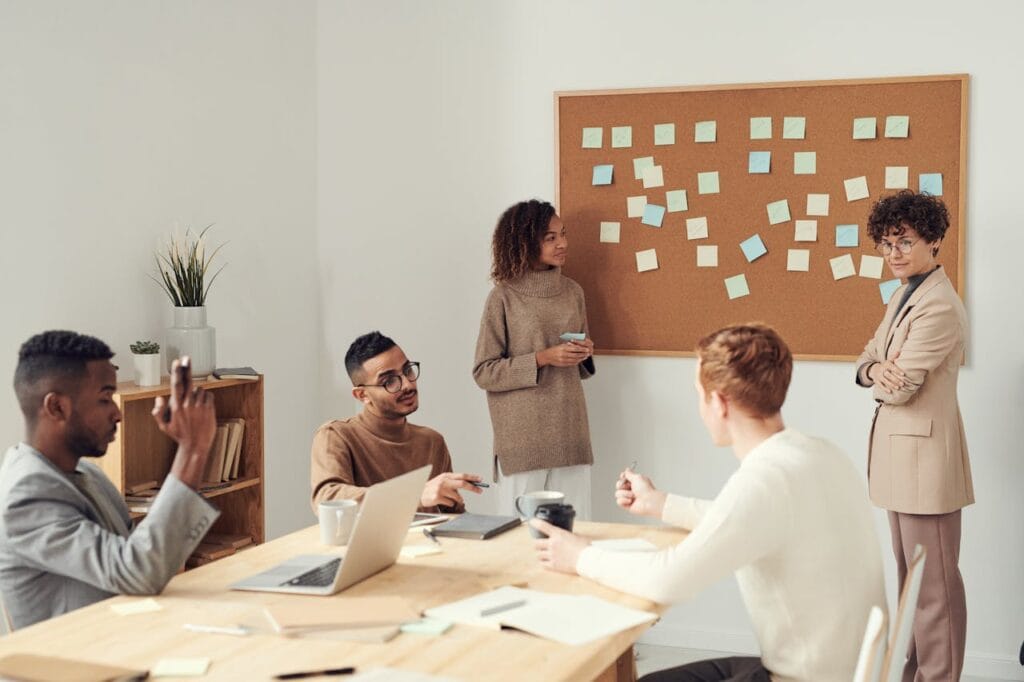 Sesión de lluvia de ideas en equipo en una sala de reuniones, con un panel lleno de notas adhesivas de colores y varios compañeros compartiendo ideas y estrategias alrededor de una mesa.